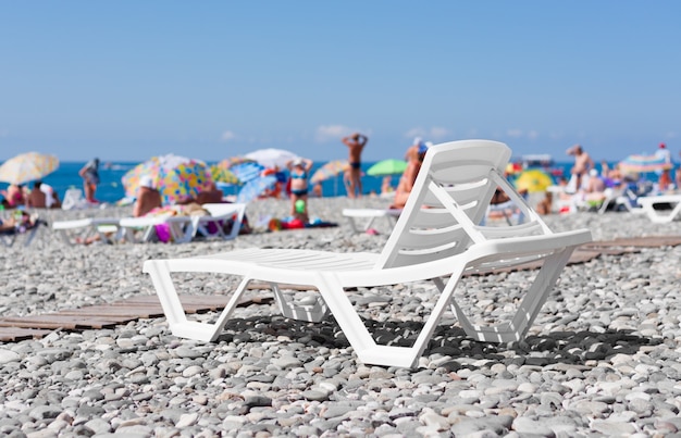 Weiße Plastikliege am Strand am Meer auf dem Hintergrund des Sonnenbadens der Leute