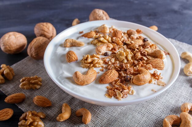 Weiße Platte mit griechischem Joghurt, Granola, Mandel, Acajoubaum, Walnüssen auf schwarzem hölzernem.