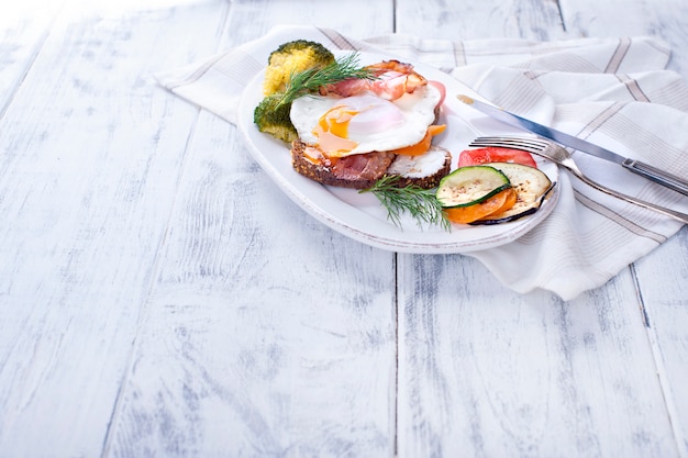 Weiße Platte mit Toast mit Speck und Gemüse und Spiegelei