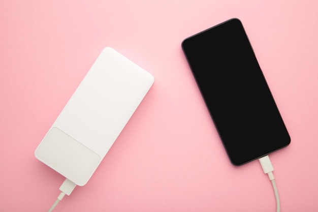 Weiße Powerbank lädt Smartphone auf rosa Hintergrund auf