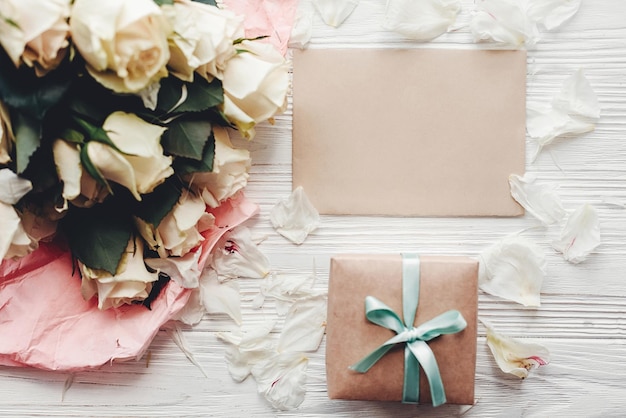Weiße Rosen mit leerer Karte und Geschenkbox auf Holzhintergrund flach mit Platz für Text Blumengrußkarte Mockup Hochzeitseinladungglückliches Muttertagskonzept Valentinstag xA