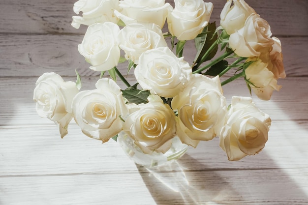Weiße Rosen stehen in einer Vase auf weißen Holzbrettern