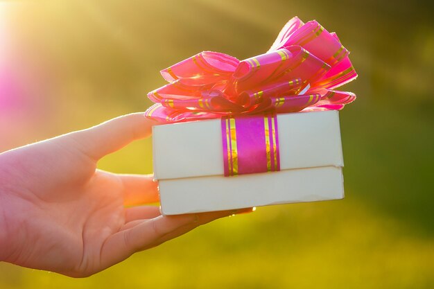 Weiße Schachtel mit rosa Schleife mit einem Geschenk in der Hand