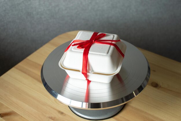 Weiße Schachtel mit rotem Band für Kuchenbento auf Gebäckmetalldrehteller für Kuchen