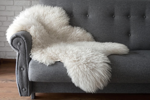Weiße Schafshaut auf einem grauen Sofa Ein gemütlicher Ort zum Entspannen in der Wohnung Modernes Interieur im skandinavischen Stil