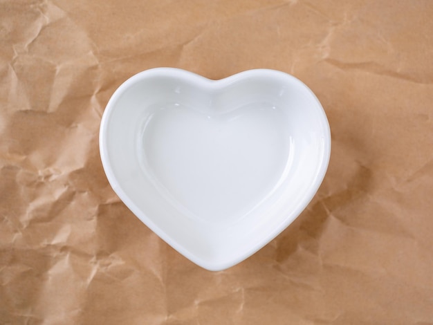 Weiße Schüssel in Form eines Herzens auf dem Hintergrund von zerknittertem Bastelpapier