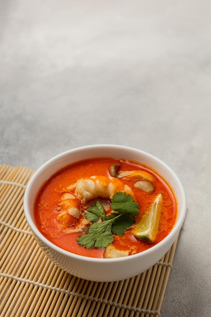 Weiße Schüssel mit frischer Tom Yum-Suppe auf einem Bambusständer auf hellem Hintergrund