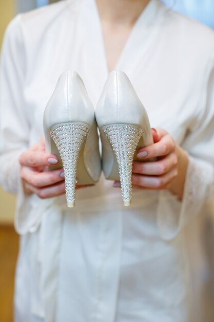Weiße Schuhe mit Absätzen in den Händen der Braut