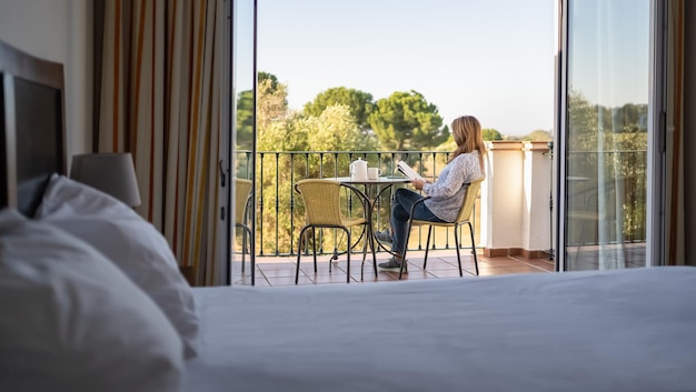 Weiße Seniorin liest im Urlaub ein Buch auf der Terrasse ihres Hotelzimmers