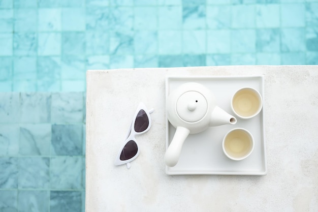 Weiße Sonnenbrille und heiße Teekanne in der Nähe des Swimmingpools im Luxushotel Sommerreise Urlaub Urlaub und Wochenendkonzept