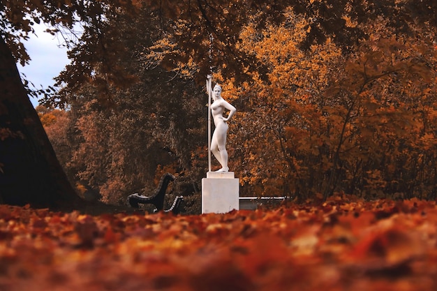 Weiße Statue eines Mädchens mit einem Paddel in einem dunklen Herbstpark viele Blätter auf dem Boden