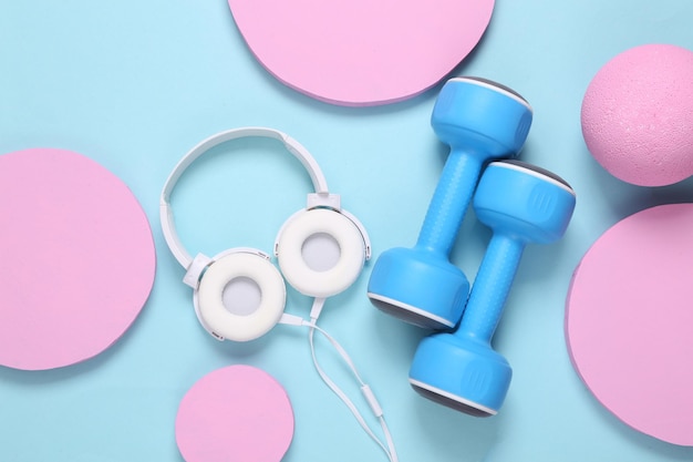 Weiße Stereokopfhörer und Hanteln auf blauem Hintergrund mit rosa Kreisen Minimalistisches, modernes Fitness-Layout