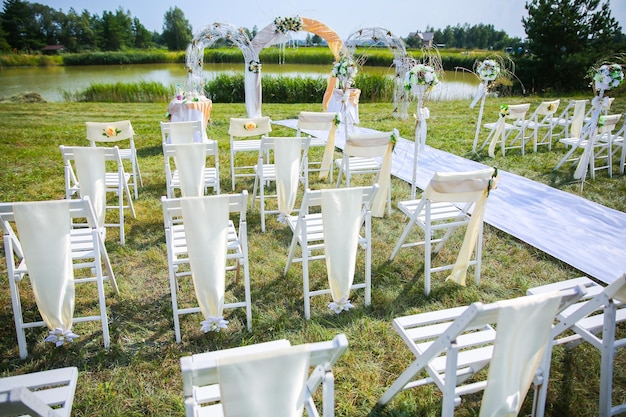 Weiße Stühle und Bogen mit Blumen bei der Hochzeitszeremonie im Freien