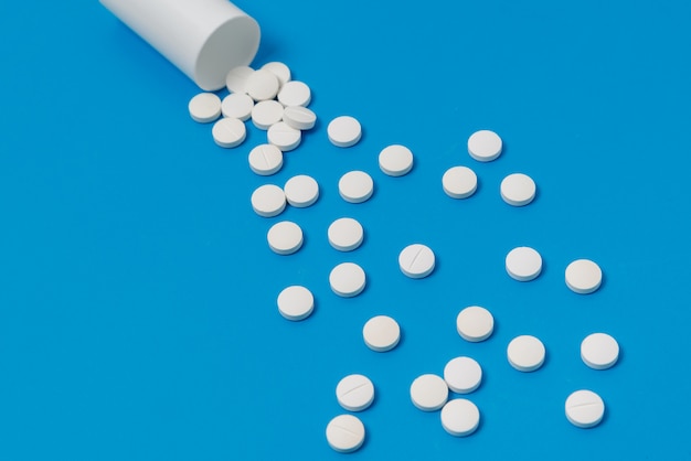 Weiße Tabletten und Flasche für Tabletten auf blauer Oberfläche