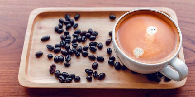 Weiße Tasse Espressokaffee und geröstete Kaffeebohnen auf einem Holztablett