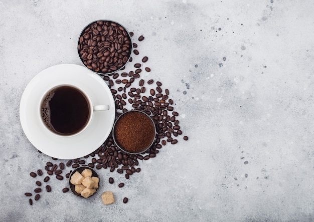 Weiße Tasse frischer roher Bio-Kaffee mit Bohnen und gemahlenem Pulver mit Rohrzuckerwürfeln mit Kaffeebaumblatt auf hellem Hintergrund. Ansicht von oben