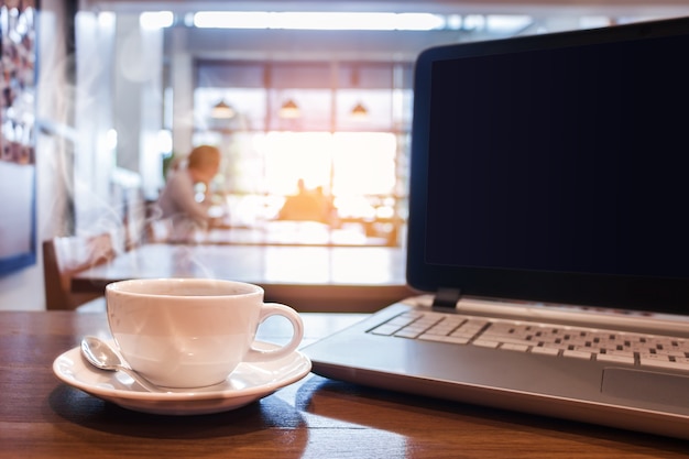 Weiße Tasse heißen Kaffee mit Laptop auf Holztisch im Café.