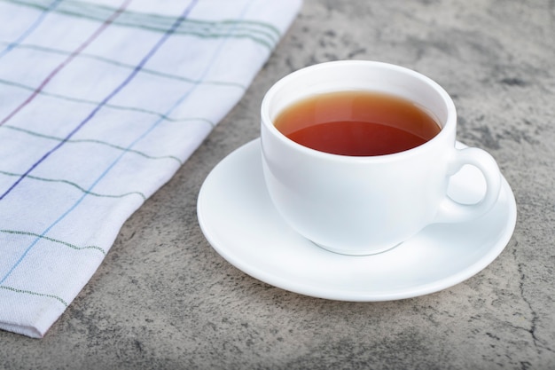 Weiße Tasse heißen Tees mit weißer Tischdecke auf Steinhintergrund.