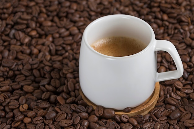 weiße Tasse Kaffee auf dem Hintergrund der Kaffeebohnen.