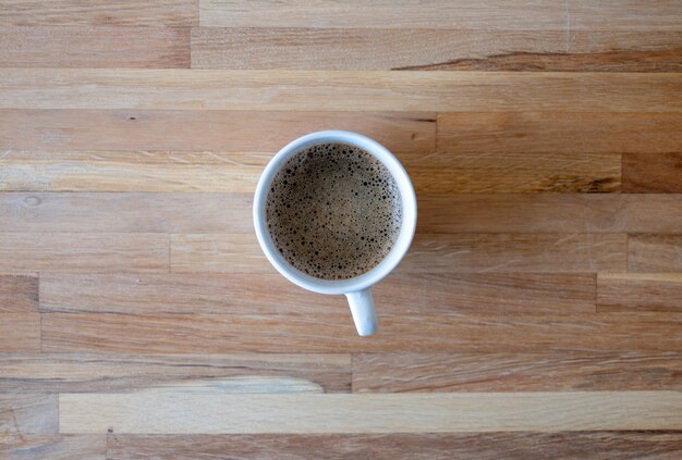 Weiße Tasse Kaffee auf Holzhintergrund von oben