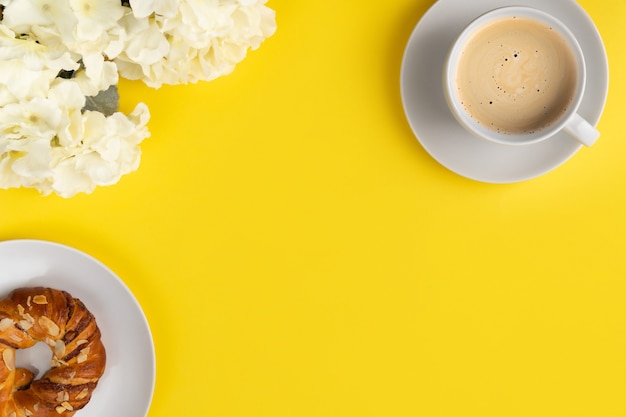 Weiße Tasse Kaffee und Blumen auf gelbem Hintergrund. Flat Lay Draufsicht Frühstückskonzept