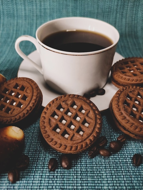 Weiße Tasse Kaffee und runde braune Kekse auf blauem Hintergrund