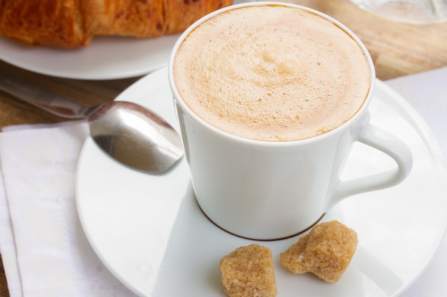 Weiße Tasse mit frischem Espressokaffee und Croissant hautnah