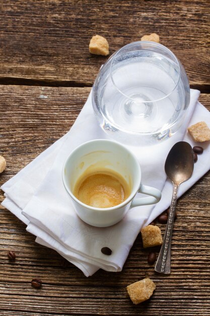Weiße Tasse mit getrunkenem frischem Espressokaffee und Glas Wasser auf Holz
