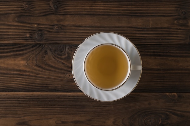 Weiße Tasse mit grünem Tee auf einem Holztisch. Ein belebendes Getränk, das für die Gesundheit nützlich ist.