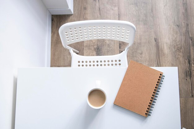 Weiße Tasse mit Kaffee-Notizbuch auf einem weißen Tisch unter natürlichem Licht Draufsicht flach gelegt