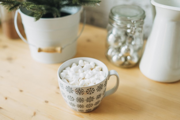 Weiße Tasse mit Kakao oder Kaffee mit Marshmallow auf dem Küchentisch Weihnachtsstimmung gemütliches Zuhause