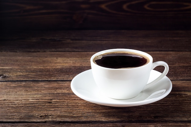 Weiße Tasse mit schwarzem Kaffee auf Holztisch