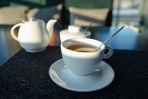 Weiße Tasse mit Wasserkocher auf Café-Tisch-Sonnenunterganglicht