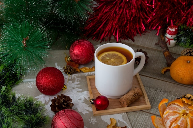 Weiße Tasse mit Zitronentee auf einem hölzernen Becherhalter, Neujahrsdekor, rote Weihnachtsdekoration, Tannenzweige, Weihnachtshintergrund