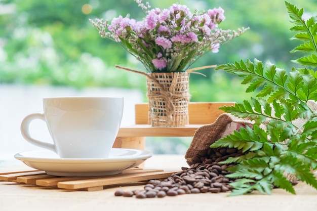 Weiße Tasse schwarzer Kaffee oder Tee auf Holzplatte über verschwommene Kaffeebohne