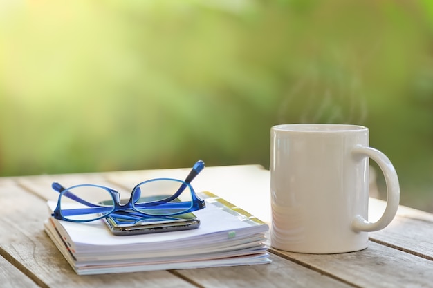 Weiße Tasse Tasse heißen Kaffees mit Buch, Notizbuch und Lesebrille