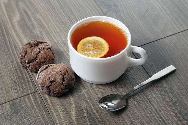 Weiße Tasse Tee mit Zitrone, Teelöffel und Keksen auf einem Holztisch