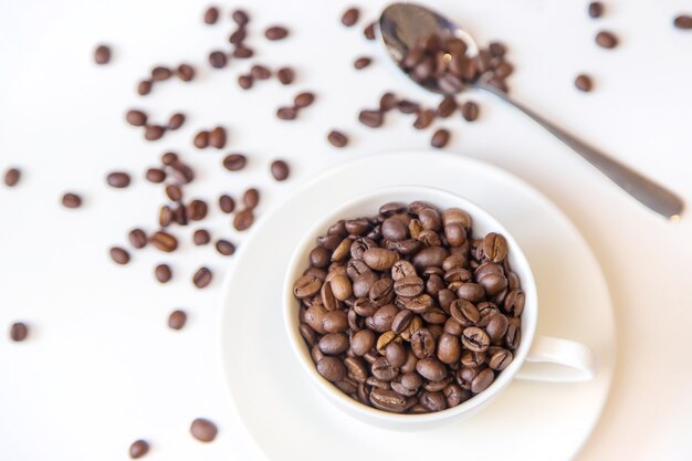 Weiße Tasse und Kaffeebohnen auf weißem Hintergrund. Selektiver Fokus.