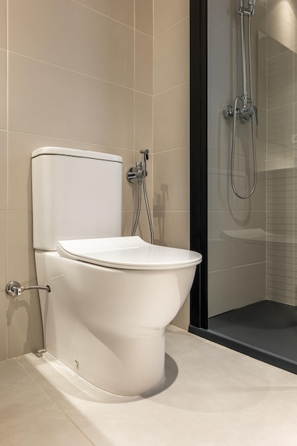 Weiße Toilettenschüssel mit Bidetdusche mit Wandhalterung in einem modernen Badezimmer mit Dusche
