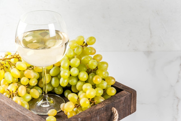 Weiße Trauben und Weißwein in einem Glas, in einem hölzernen Behälter auf einer weißen Marmortabelle. Kopieren Sie Platz