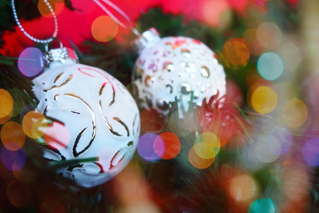 Weiße trendige Weihnachtskugeln mit Streuseln und einem Muster auf den Weihnachtsbaumzweigen Mehrfarbiges schönes Bokeh um die Dekorationen Postkarten- oder Neujahrs-Weihnachtshintergrund Festliche Stimmung