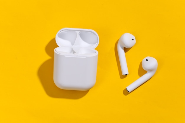 Weiße True-Wireless-Bluetooth-Kopfhörer oder -Ohrhörer mit Ladehülle auf gelbem, hellem Hintergrund.