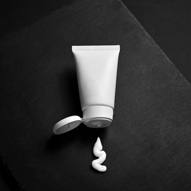 Weiße Tube mit ausgepresster Creme auf schwarzem Hintergrund Kreatives Kosmetikfoto