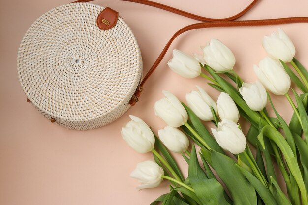 Weiße Tulpen und Frauengeflecht runde Handtasche auf einem rosa Hintergrund