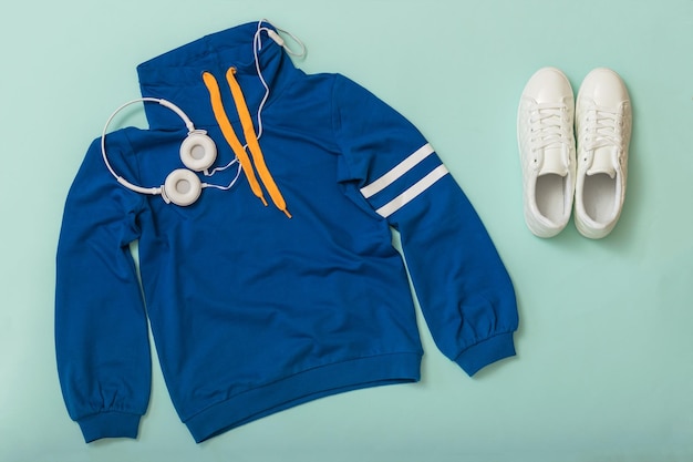 Weiße Turnschuhe, weiße Kopfhörer und eine stylische Sportjacke auf blauem Grund. Sport-Lifestyle-Accessoires.