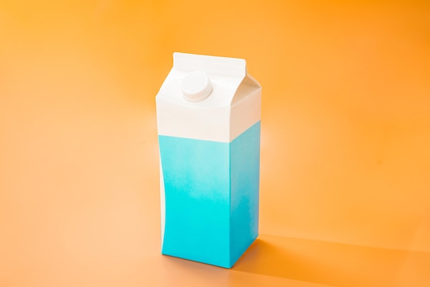 Foto weiße und blaue papierpackung milch steht auf orangefarbenem hintergrund ernährung geschlossene plastikkappe nährstoff kuh design mockup werbung seitenansicht