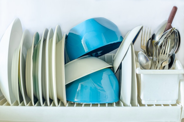 Foto weiße und blaue teller zum essen, besteckgabeln, messer, löffel in einem glas zum trocknen von geschirr in der küche o