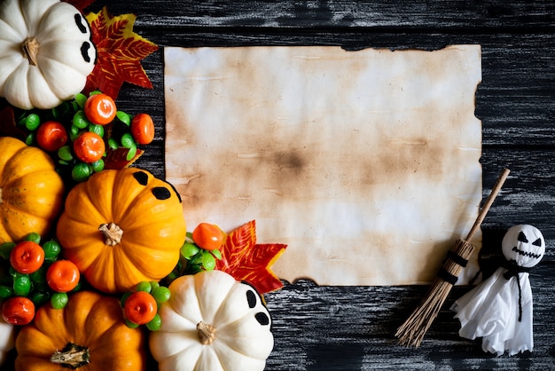 Weiße und gelbe Geistkürbise mit Herbstlaub und altem Papier auf einem schwarzen hölzernen backgro