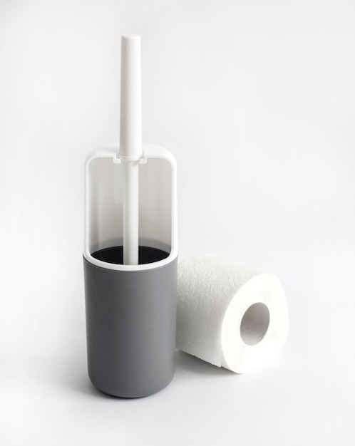 Weiße und graue Plastiktoilettenbürste und Toilettenpapier auf weißer Oberfläche