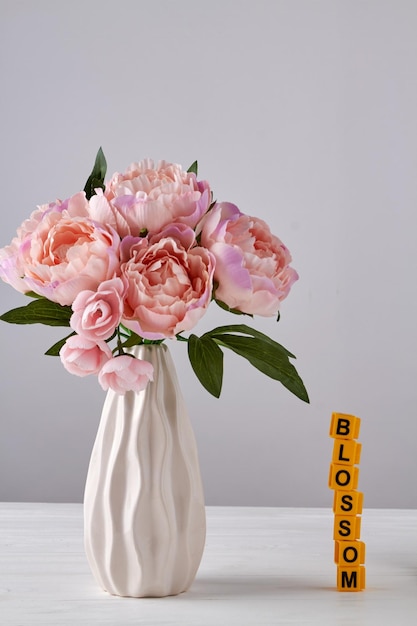 Weiße Vase mit rosafarbenen Pfingstrosen auf weißem Hintergrund Stapel gelber Buchstabenwürfel, die in Blosso angeordnet sind